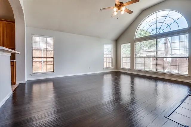 an empty room with wooden floor chandelier and windows