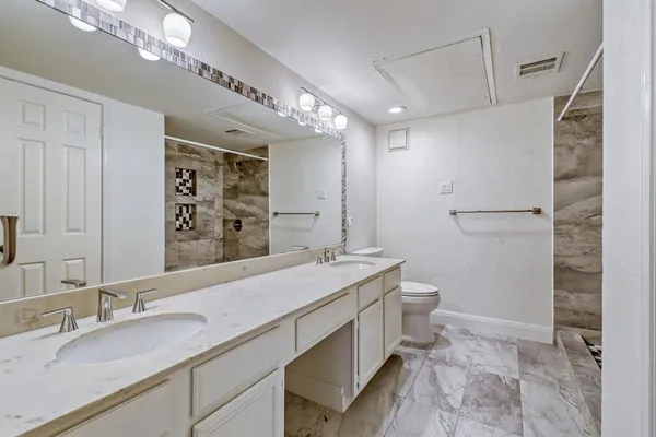 a bathroom with a granite countertop sink a toilet a mirror and shower
