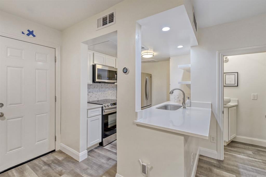 8750 Park Lane, Unit 142 Dallas, TX 75231 - Photo 2 of 17 Kitchen featuring stainless steel appliances, white cabinets, backsplash, light wood finished floors, and light stone countertops
