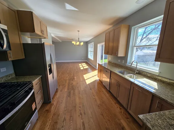 a kitchen with granite countertop a stove a sink dishwasher a refrigerator and wooden floor