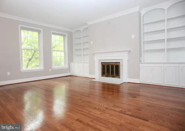 an empty room with wooden floor fireplace and windows