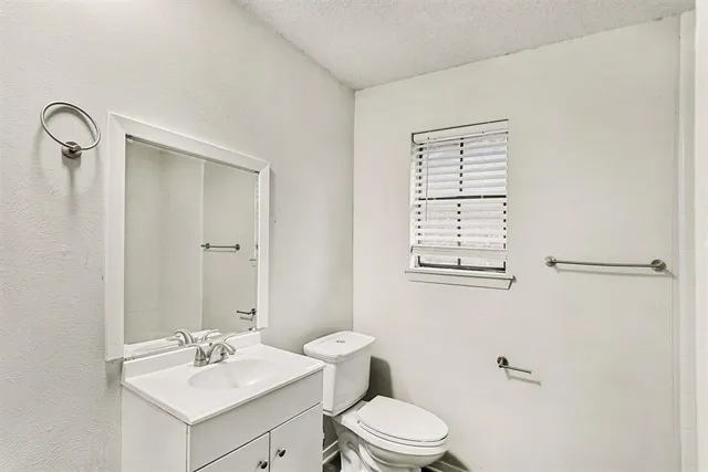 a bathroom with a toilet a sink a mirror a window and vanity