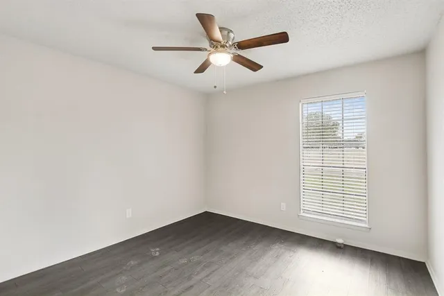 an empty room with wooden floor ceiling fan and windows