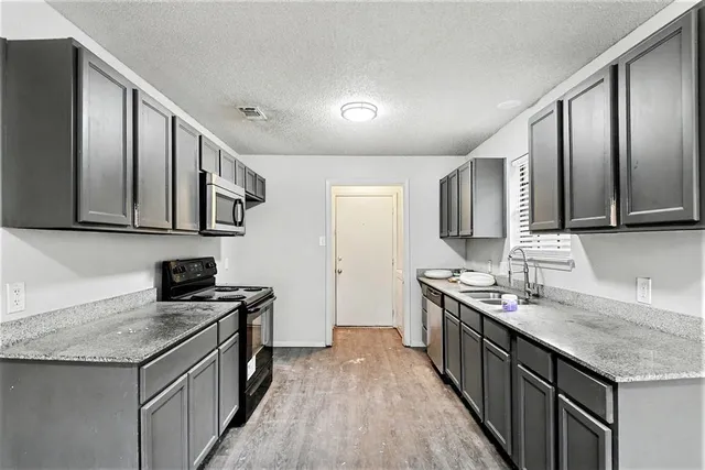 a kitchen with granite countertop stainless steel appliances a sink stove top oven and cabinets