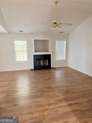 an empty room with wooden floor fireplace and windows