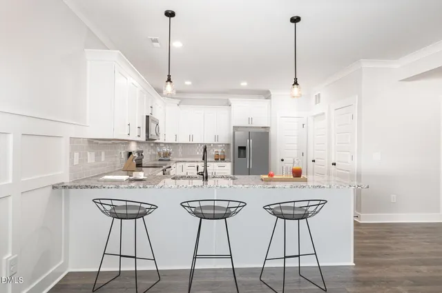 a view of a kitchen with stainless steel appliances kitchen island granite countertop a dining table chairs and white cabinets