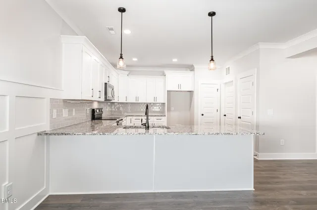 a kitchen with stainless steel appliances kitchen island granite countertop a refrigerator a sink and white cabinets