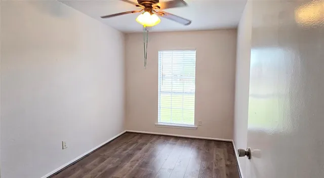 an empty room with wooden floor fan and windows