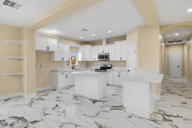 a kitchen with granite countertop a sink a stove a refrigerator and white cabinets with wooden floor