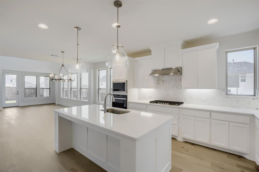 828 Stone Grv Road Lavon, TX 75166 - Photo 4 of 27 Modern kitchen featuring a large island with sink, white cabinetry, integrated stainless steel appliances, and a gas cooktop