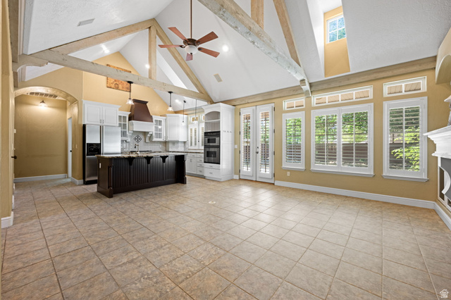 20 Valley Road Leeds, UT 84746 - Photo 7 of 57 Spacious open-concept living area featuring a vaulted ceiling with exposed wood beams, a central kitchen island with seating, a built-in double oven, multiple windows with plantation shutters, and light-toned tile flooring