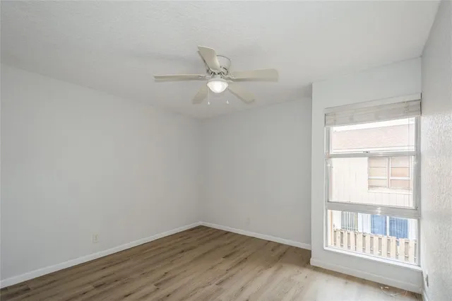 an empty room with wooden floor fan and windows