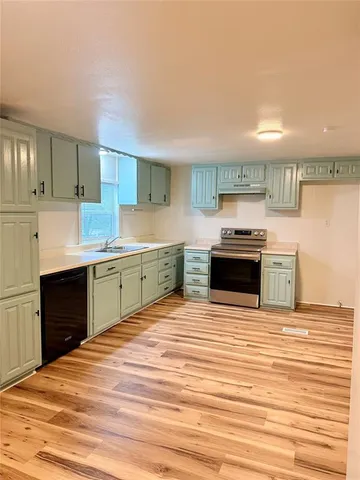 a large kitchen with stainless steel appliances a large kitchen island a stove a refrigerator white cabinets and wooden floor