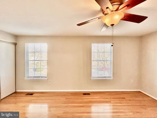 an empty room with wooden floor ceiling fan and windows