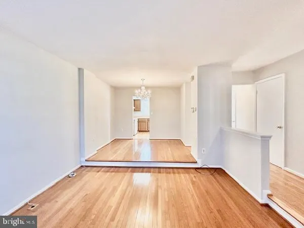 a view of empty room with wooden floor and kitchen
