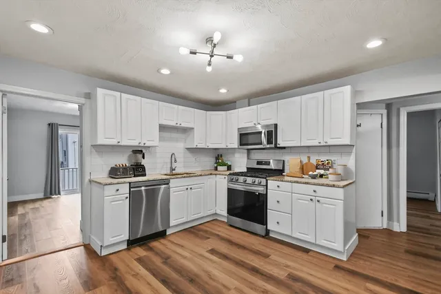 a kitchen with stainless steel appliances granite countertop a stove top oven a sink dishwasher and a refrigerator with wooden floor