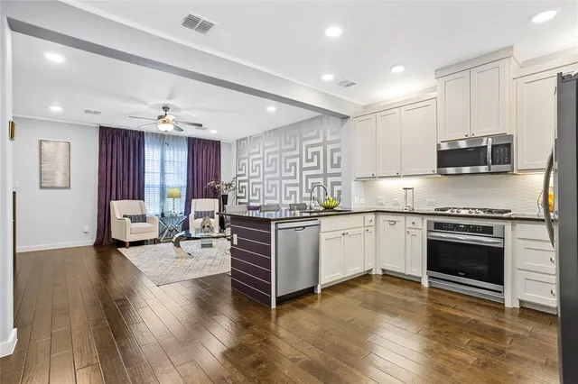 a kitchen with stainless steel appliances kitchen island granite countertop a stove top oven a sink dishwasher a dining table and chairs with wooden floor
