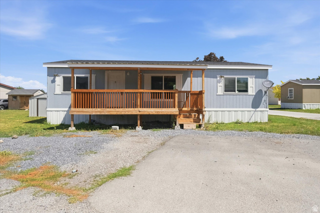 433 North 750 West Logan, UT 84321 - Photo 2 of 40 Light blue siding mobile home featuring a covered front porch with natural wood railings, white window shutters, and a gravel front area