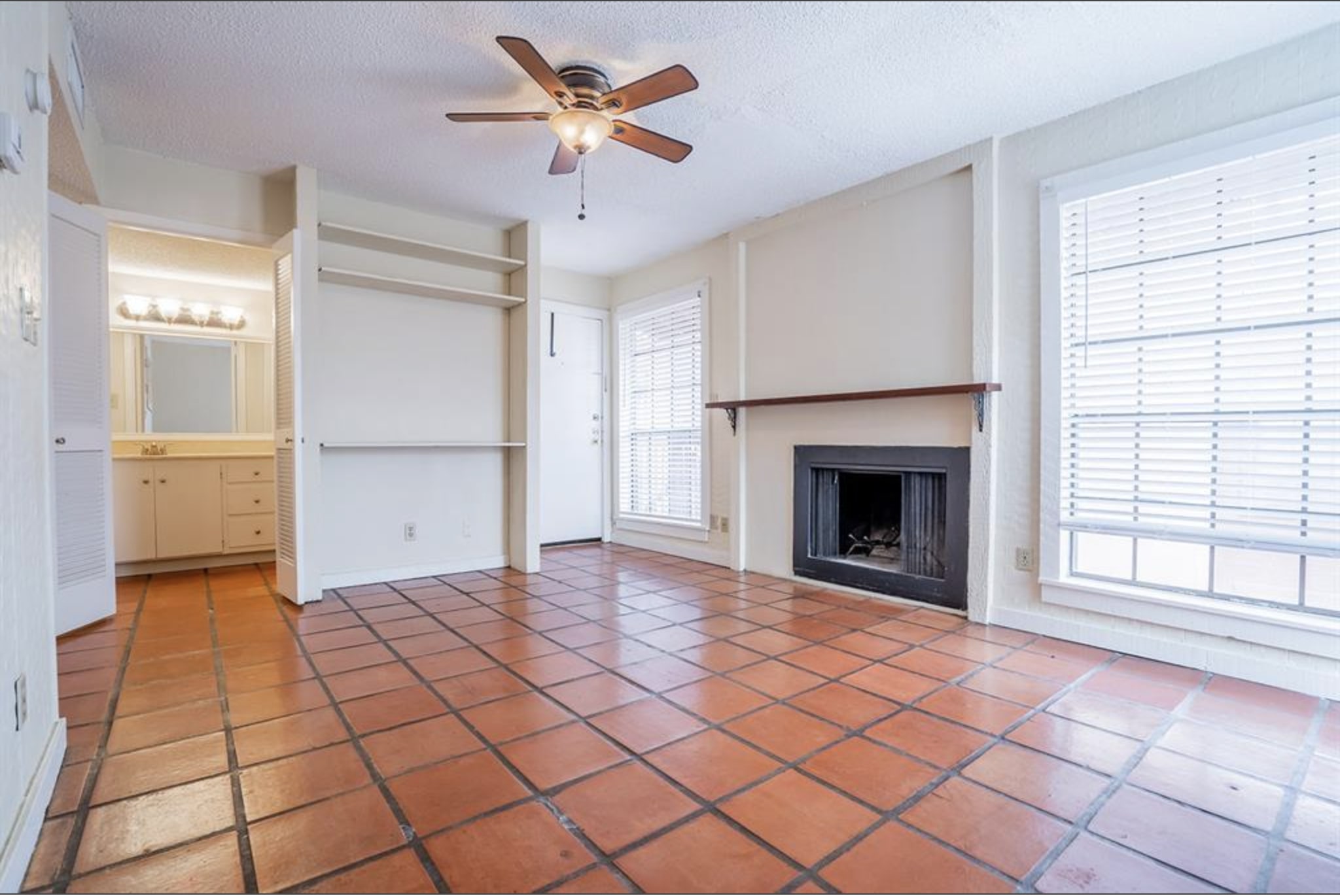 a view of a livingroom with a fireplace a ceiling fan and windows
