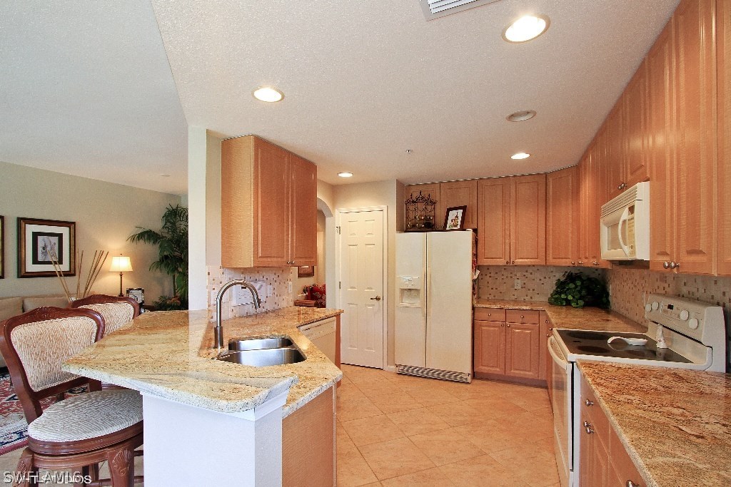 10110 Valiant Court, Unit 101 Fort Myers, FL 33913 - Photo 5 of 25 a kitchen with a refrigerator a stove top oven a sink dishwasher and white cabinets with wooden floor