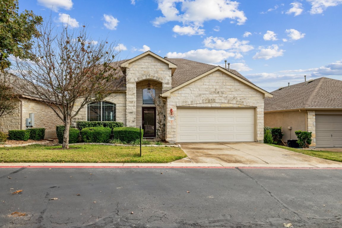 French provincial home featuring stone siding, a front yard, driveway, and a garage