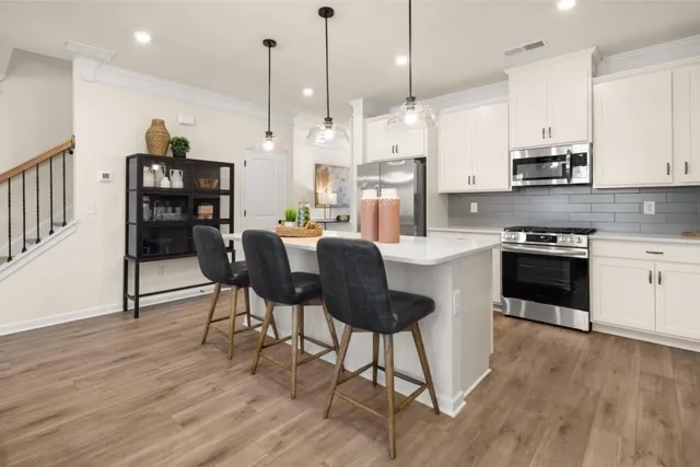 a kitchen with stainless steel appliances granite countertop a stove a refrigerator a kitchen island a dining table and chairs with wooden floor