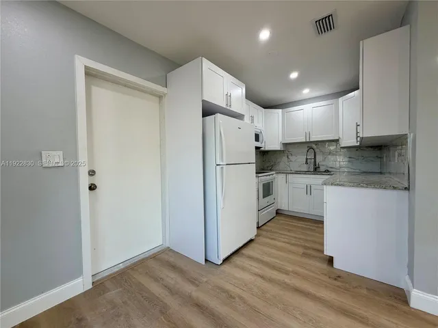 a kitchen with granite countertop a refrigerator a sink and white cabinets