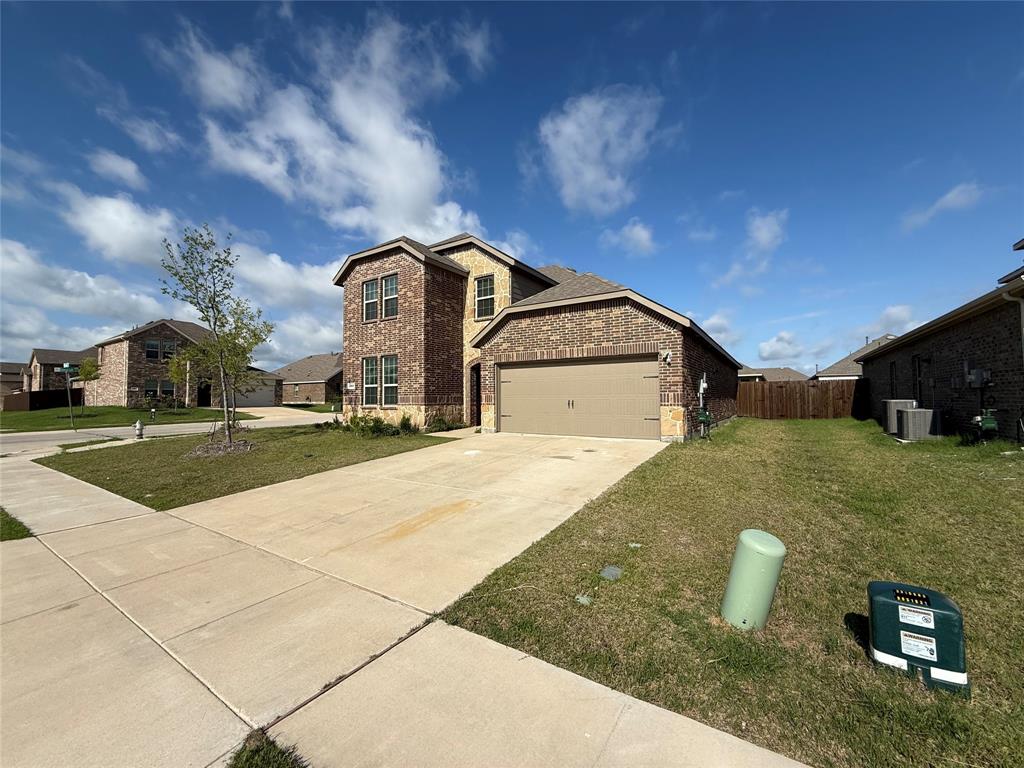1306 Colonial Bluff Lane Princeton, TX 75407 - Photo 4 of 27 Two-story brick and stone facade residence featuring an attached two-car garage with a tan door, a concrete driveway, and a sidewalk