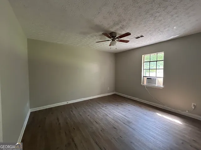 an empty room with wooden floor ceiling fan and windows
