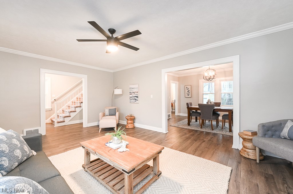 Living room with ornamental molding, light wood-type flooring, and ceiling fan with notable chandelier