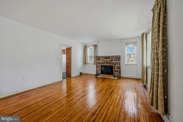 an empty room with wooden floor fireplace and windows