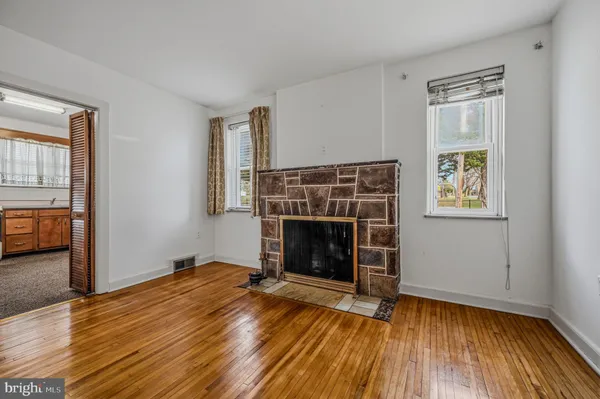 a view of an empty room with wooden floor fireplace and a window