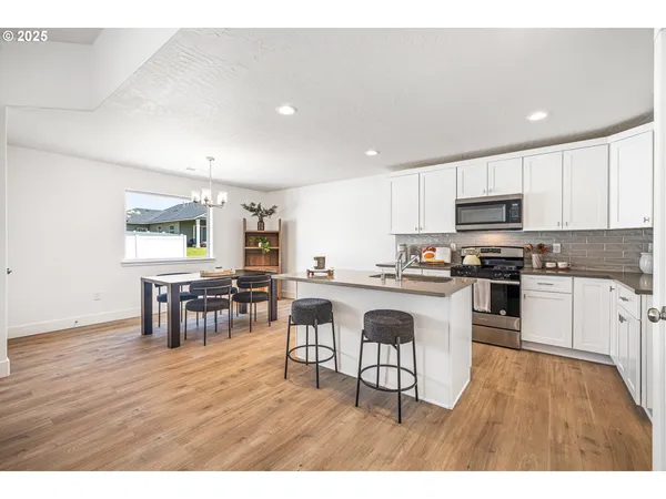 a kitchen with stainless steel appliances granite countertop a refrigerator a stove a sink and white cabinets with wooden floor