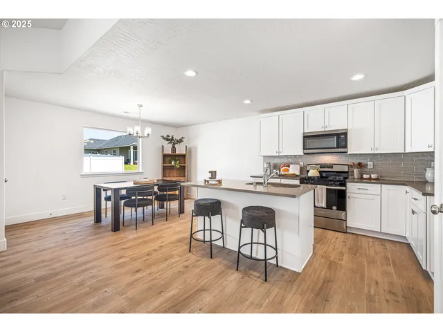 a kitchen with stainless steel appliances granite countertop a refrigerator a stove a sink and white cabinets with wooden floor