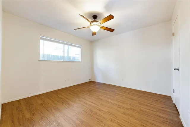 a view of an empty room with wooden floor and a ceiling fan