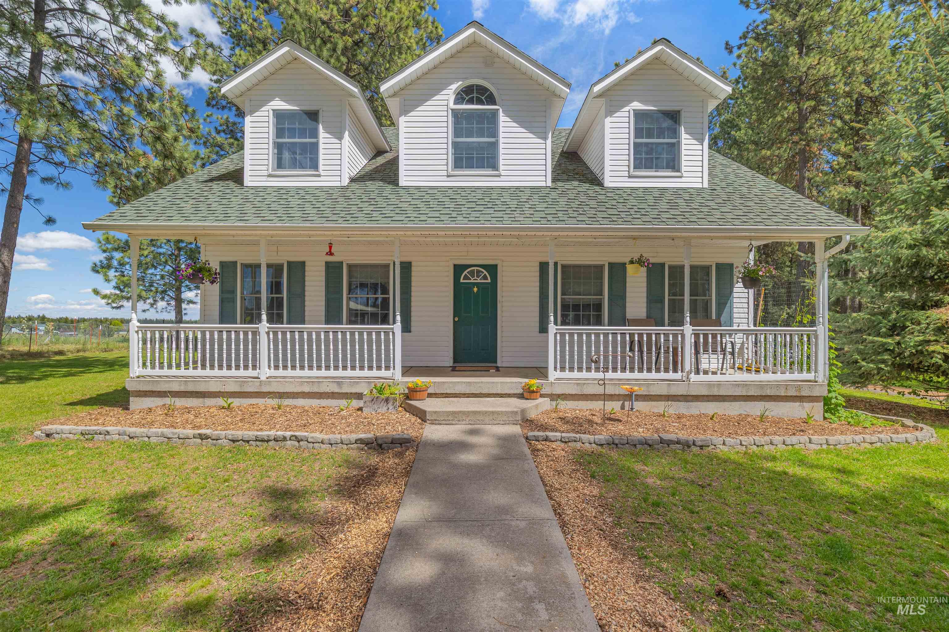 White siding exterior featuring a covered front porch with white railings, a dark green entry door, three dormer windows, and a green shingle roof