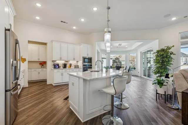 a kitchen with stainless steel appliances granite countertop a refrigerator a stove a sink and a dining table with wooden floor