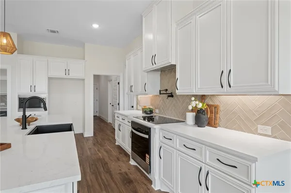 a kitchen with stainless steel appliances granite countertop a stove a sink dishwasher and white cabinets with wooden floor