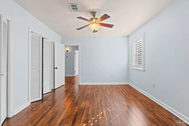 a view of an empty room with wooden floor and a ceiling fan
