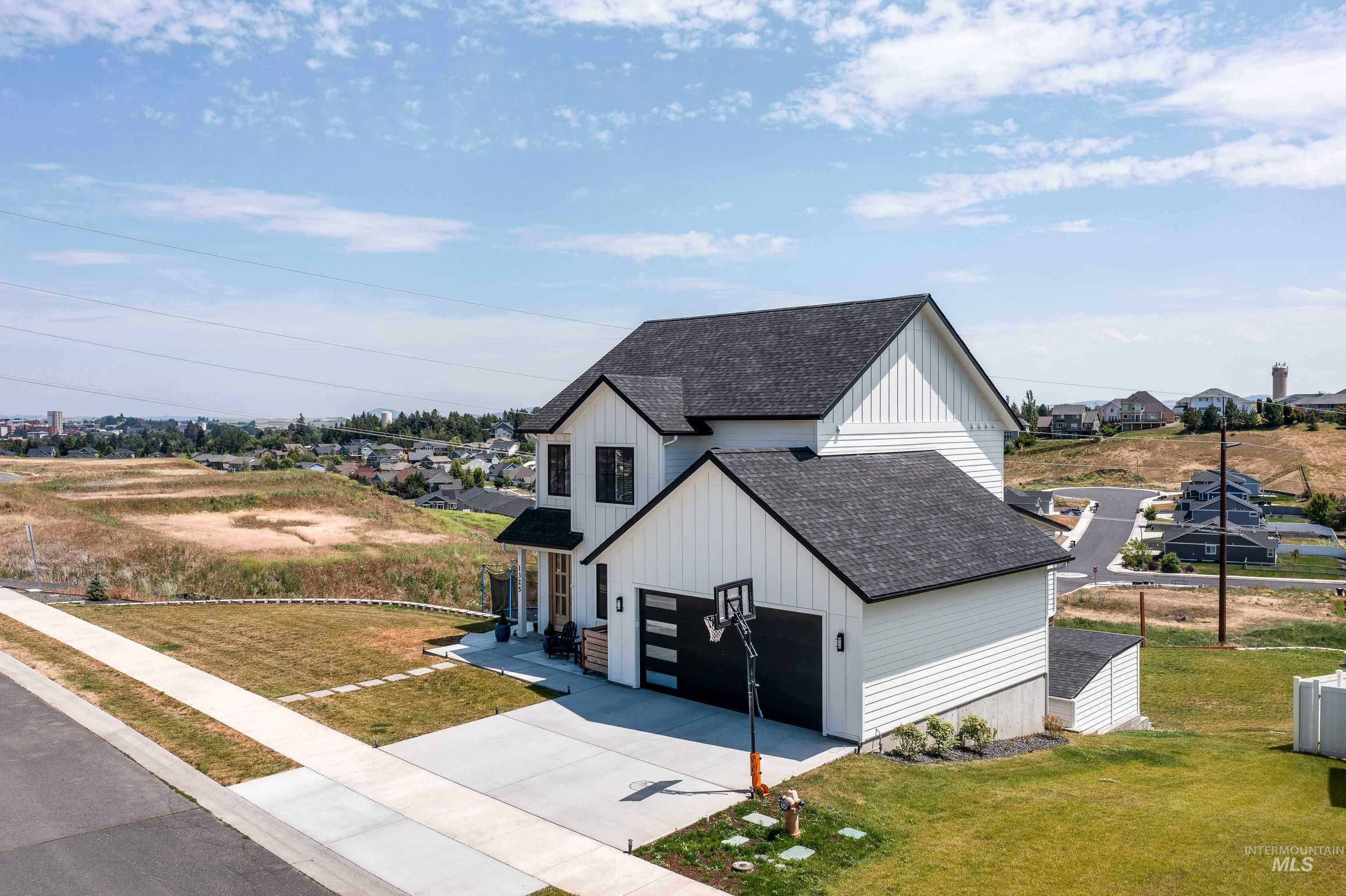1325 Southwest Panorama Drive Pullman, WA 99163 - Photo 39 of 48 View of front of house featuring a shingled roof, board and batten siding, concrete driveway, a front lawn, and a residential view
