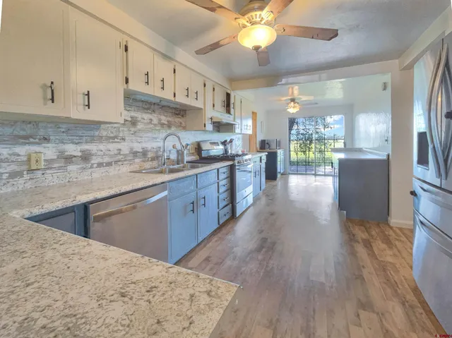 a kitchen with stainless steel appliances granite countertop a refrigerator a sink dishwasher a stove and white countertops with wooden floor