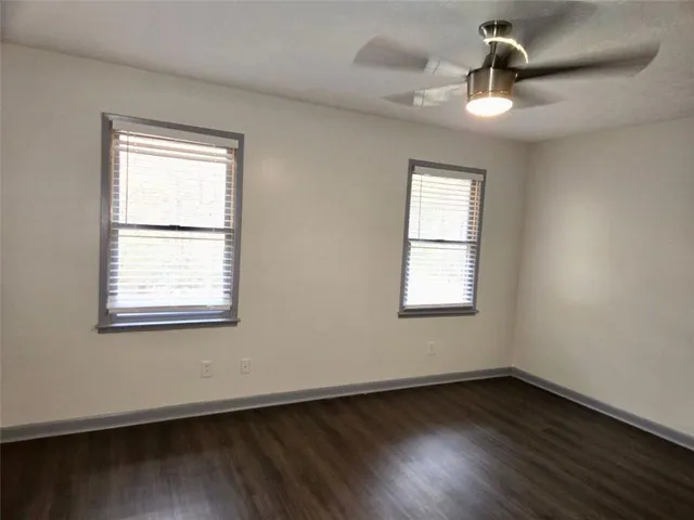 an empty room with wooden floor chandelier fan and windows