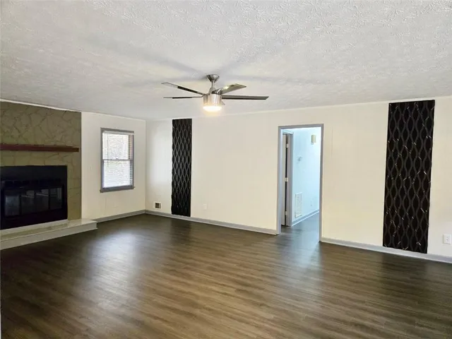 a view of an empty room with wooden floor fireplace and a window