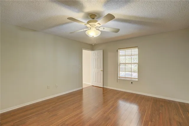 an empty room with wooden floor fan and windows