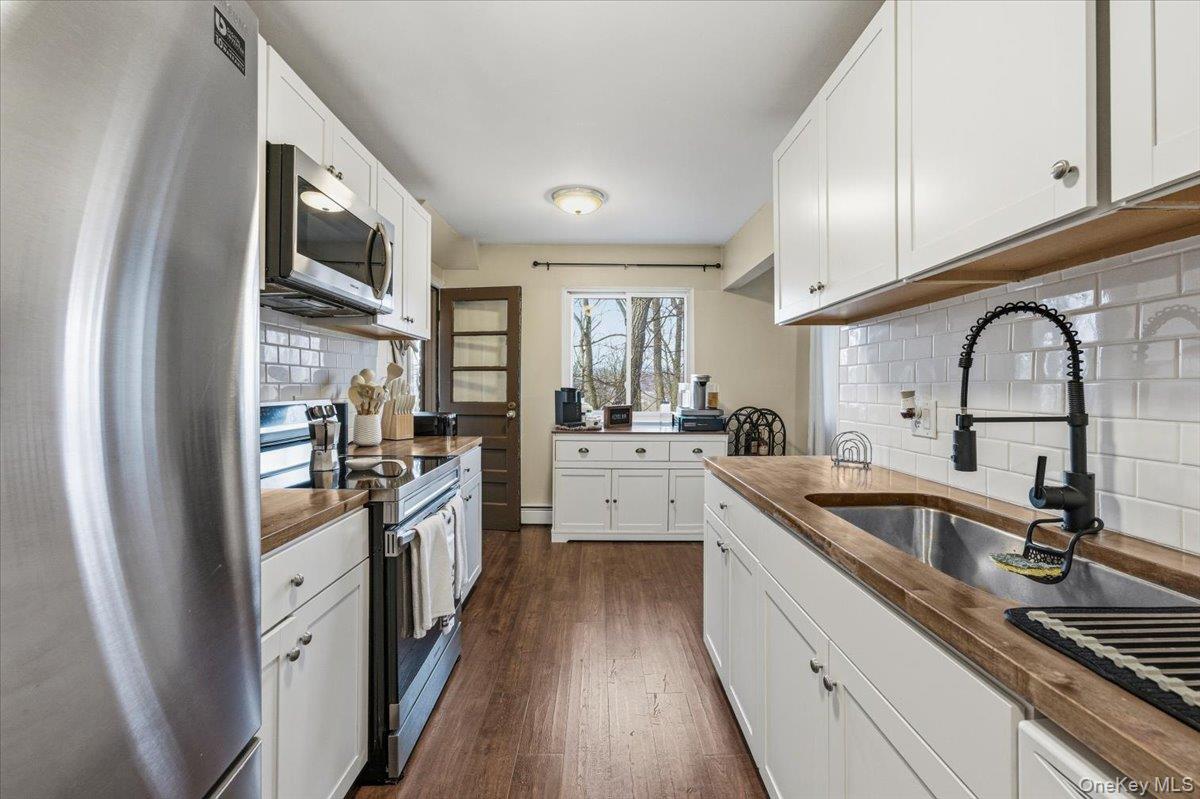 9 North James Street, Unit B Peekskill, NY 10566 - Photo 6 of 22 Kitchen with appliances with stainless steel finishes, white cabinetry, dark wood-type flooring, and backsplash