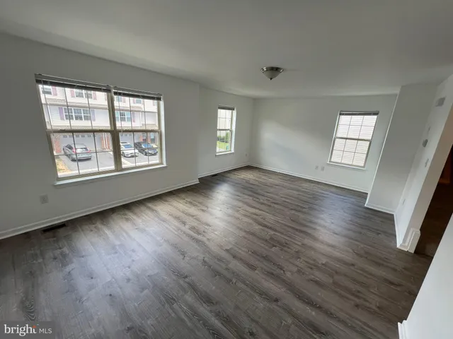 a view of an empty room with wooden floor and window