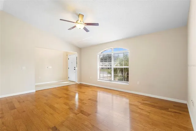 an empty room with wooden floor fan and windows