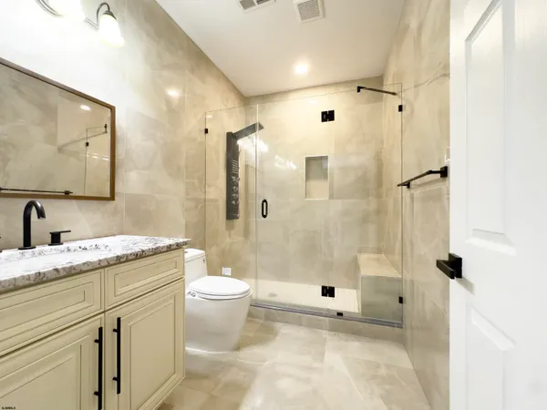 a bathroom with a granite countertop sink a toilet a mirror and shower