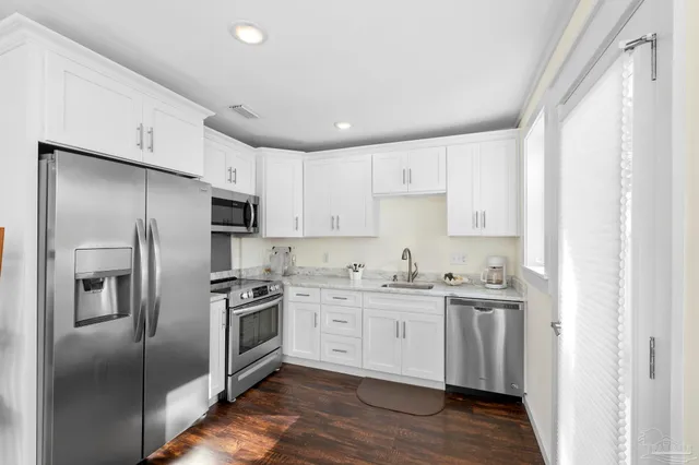 a kitchen with stainless steel appliances granite countertop a refrigerator a sink a stove and white cabinets with wooden floor