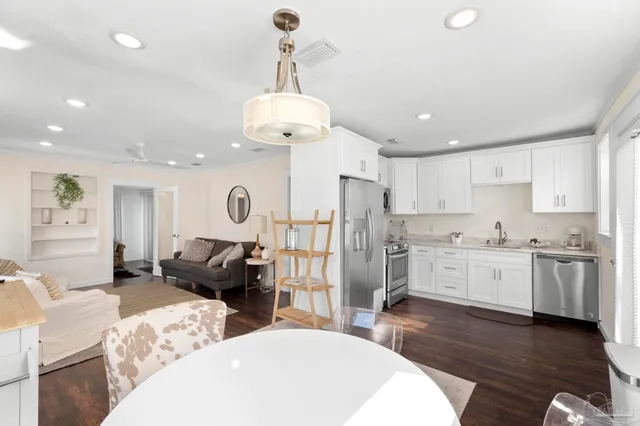 a open kitchen with stainless steel appliances granite countertop a refrigerator a stove a sink dishwasher a dining table and chairs with wooden floor